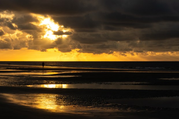 A picture of a polarized sunrise at Hilton Head Island with emphasis on the golden morning light. A silhouette of a person walking can be seen along the shoreline.